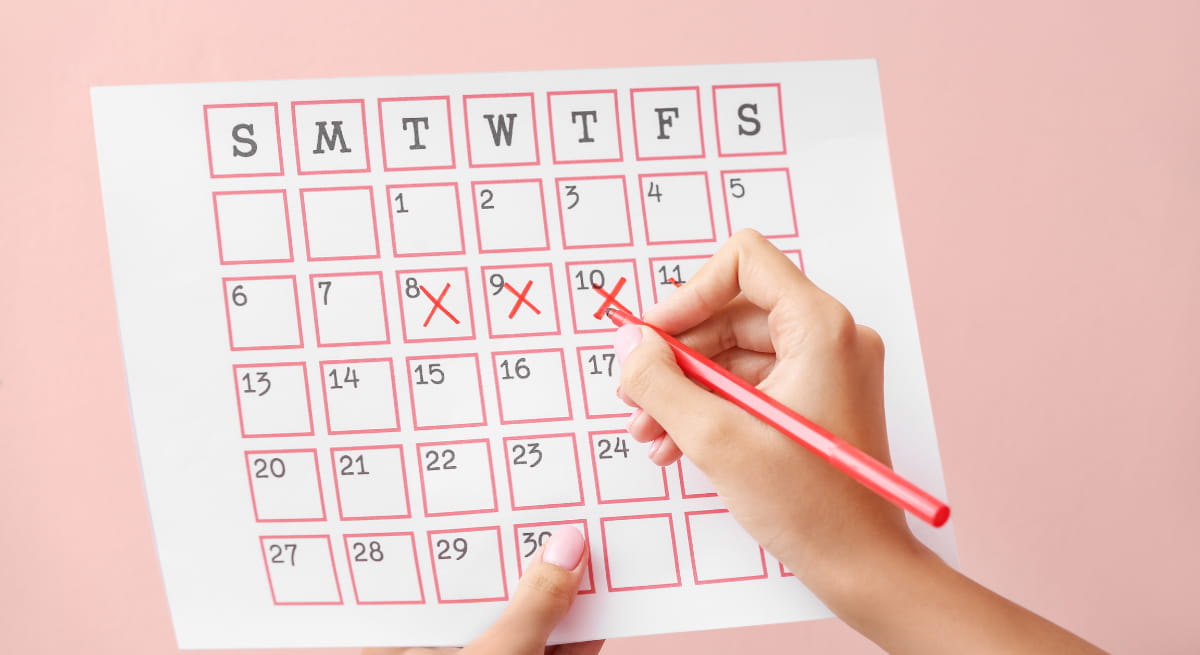Close-up of a hand marking dates on a paper wall calendar with irregular circles and notes